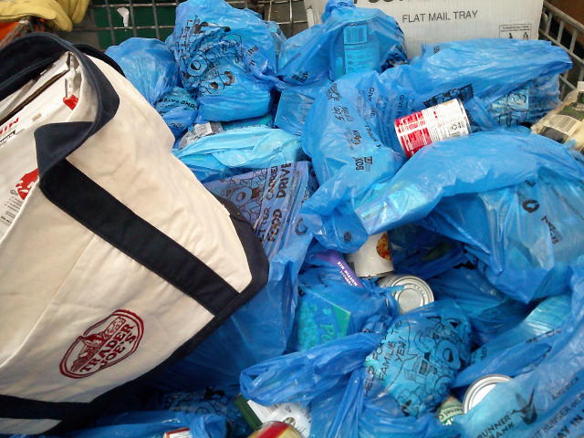 Mail tray and trader joe bag on top of plastic bag of food in a mail cart.